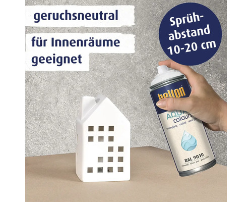 Eine Hand sprüht mit Belton Aqua Sprayfarbe ein weißes Deko Haus. Das Produkt ist geruchsneutral, für Innenräume geeignet und RAL 9010 seidenmatt.