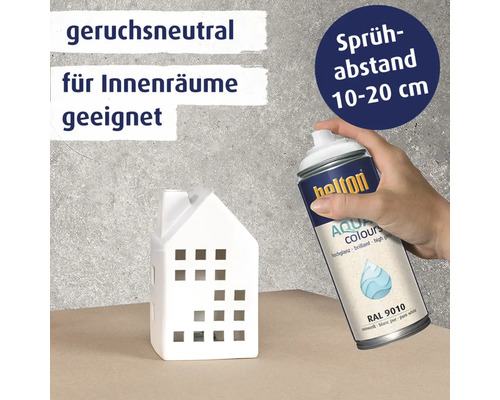 Eine Hand hält eine Sprühdose Belton Aqua Colours Lack, um ein kleines Haus aus Keramik zu besprühen, mit Hinweisen zu Geruchsneutralität und Abstand.