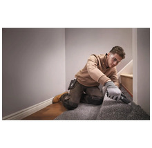 Handwerker mit Schutzbrille und Handschuhen beim Zuschneiden von Teppichboden auf einer Treppe mit einem Teppichmesser.