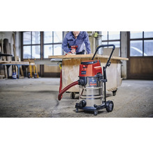 Einhell Nass Trockensauger mit Edelstahlbehälter im Einsatz in einer Werkstatt mit Handwerker im Hintergrund.