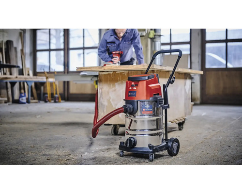 Einhell Nass Trockensauger mit Edelstahlbehälter im Einsatz in einer Werkstatt mit Handwerker im Hintergrund.