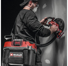 Handwerker mit Einhell Akku Wand- und Deckenschleifer und angeschlossenem Akku-Nass-Trockensauger bei der Bearbeitung einer Wand.