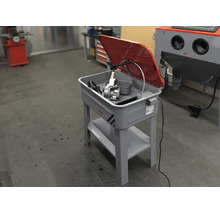 Teilereiniger auf einem Metallständer mit klappbarem Deckel und integrierter Pumpe für Werkstattarbeiten.