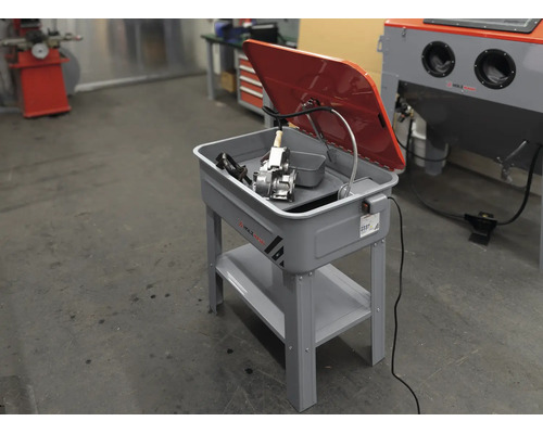 Teilereiniger auf einem Metallständer mit klappbarem Deckel und integrierter Pumpe für Werkstattarbeiten.