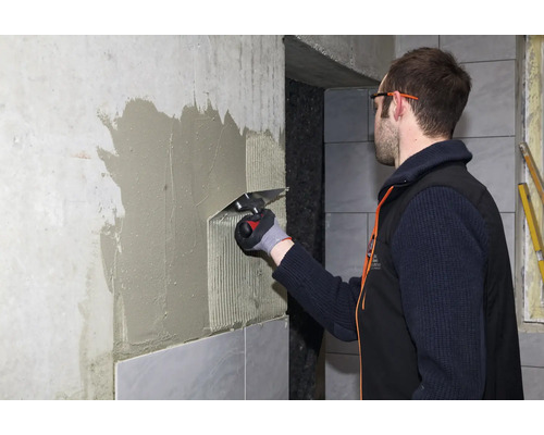 Handwerker beim Auftragen von Fliesenkleber mit einer Zahnkelle an einer Wand für die anschließende Verlegung von Fliesen.