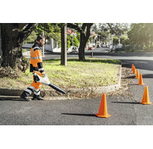 Arbeiter in Warnkleidung nutzt Stihl Laubbläser für die professionelle Straßenreinigung entlang einer Verkehrsabsicherung mit Leitkegeln.