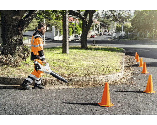 Arbeiter in Warnkleidung nutzt Stihl Laubbläser für die professionelle Straßenreinigung entlang einer Verkehrsabsicherung mit Leitkegeln.