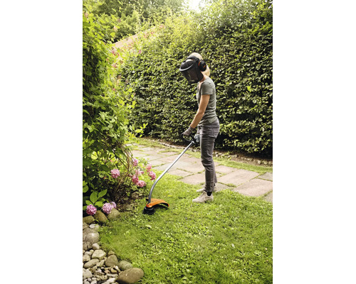 Eine Person benutzt einen Stihl Rasentrimmer mit Schutzvisier und Gehörschutz, um Kanten in einem Garten zu schneiden.