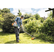 Eine Person mit Schutzhelm und Visier nutzt eine Stihl Motorsense, um Gras in einem Garten zu schneiden.