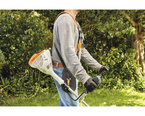 Person trägt einen Stihl Motorsensen Tragegurt bei der Arbeit mit einem Freischneider in einem Garten.