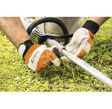 Eine Person montiert ein Stihl KombiWerkzeug an einen Stihl KombiMotor Schaft mit Handschuhen in einer Gartenumgebung.