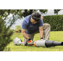 Ein Mann kniet auf einem Rasen und montiert oder wartet ein Stihl Laubblasgerät im Garten.