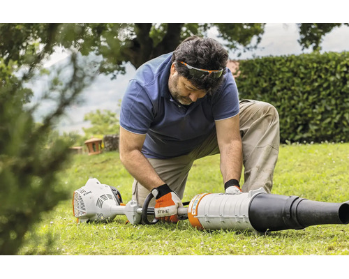 Ein Mann kniet auf einem Rasen und montiert oder wartet ein Stihl Laubblasgerät im Garten.
