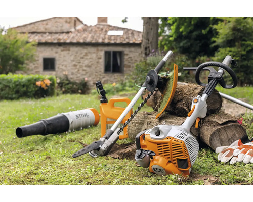 Stihl Kombimotor mit verschiedenen Aufsätzen wie Heckenschere und Laubbläser im Garten vor einem Steinhaus.