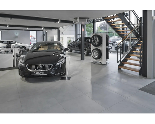 Modernes Volvo Autohaus mit Ausstellungsfahrzeugen, Reifenständer und einer Treppe in einer hellen, weitläufigen Verkaufsfläche mit Fliesenboden.