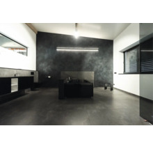 Modernes Badezimmer mit freistehender Badewanne, dunkler Wandgestaltung, großflächigen Bodenfliesen und indirekter LED Beleuchtung.