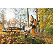 Ein Arbeiter verwendet einen Stihl Akku Laubbläser mit rückentragbarem Akku, um herbstliches Laub in einer Parkanlage zusammenzublasen.