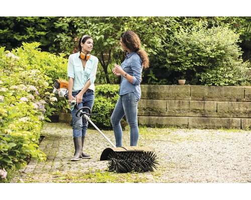 Zwei Frauen unterhalten sich im Garten neben einem Stihl Kehrwalzenvorsatz zur Reinigung von Gehwegen.