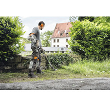 Eine Person arbeitet mit einem Stihl Freischneider an einer Mauer in einem Garten.