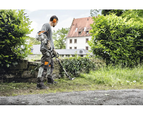 Eine Person arbeitet mit einem Stihl Freischneider an einer Mauer in einem Garten.