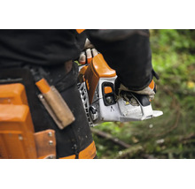 Eine Person hält eine Kettensäge in der Hand während sie Arbeitskleidung mit Holster trägt.