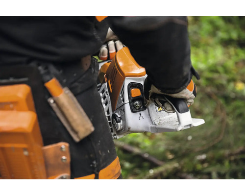 Eine Person hält eine Kettensäge in der Hand während sie Arbeitskleidung mit Holster trägt.