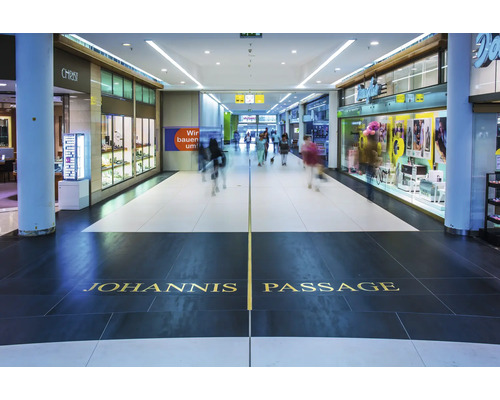 Innenansicht der Johannis Passage mit Ladenfronten und Menschen in einem modernen Einkaufszentrum.