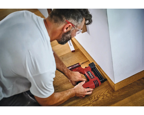 Handwerker befestigt Fußleisten mit einem Einhell Akku Nagler an der Wand.