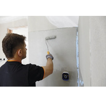 Ein Handwerker trägt mit einer Farbrolle Grundierung oder Putz auf eine Innenwand auf.