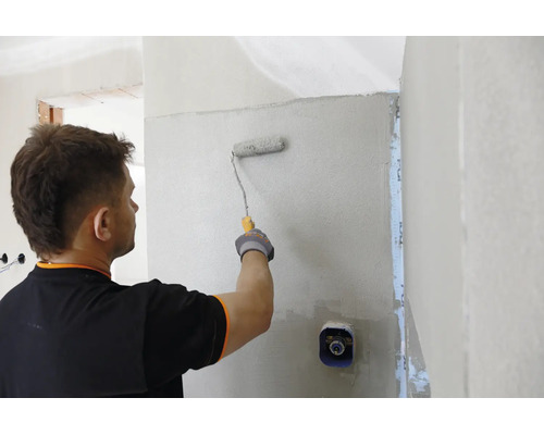 Ein Handwerker trägt mit einer Farbrolle Grundierung oder Putz auf eine Innenwand auf.