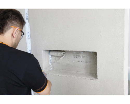 Handwerker rollt Grundierung mit einer Farbrolle in einer Wandnische mit PCI Abklebeband auf