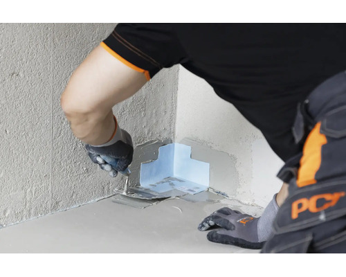 Handwerker beim Einarbeiten eines Dichtbandes in eine Innenecke mit einer Glättkelle zur professionellen Wand- und Bodenabdichtung.