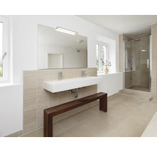 Modernes Badezimmer mit Doppelwaschbecken, Wandspiegel, Armaturen, Duschkabine und einer Holzbank vor einer hell gefliesten Wand.