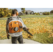 Mann trägt rückengetriebenen Stihl Benzin Laubbläser bei der Gartenarbeit um herabgefallenes Laub auf einem Rasen zu entfernen.