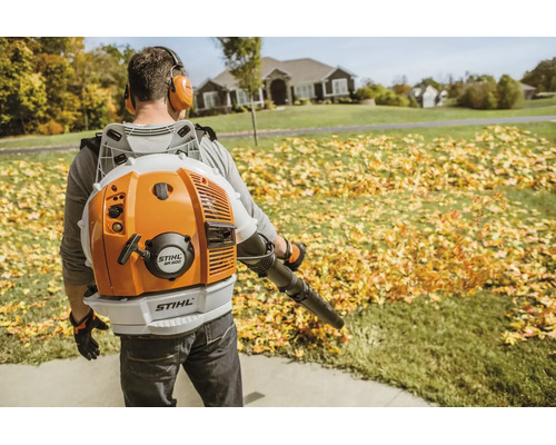 Mann trägt rückengetriebenen Stihl Benzin Laubbläser bei der Gartenarbeit um herabgefallenes Laub auf einem Rasen zu entfernen.