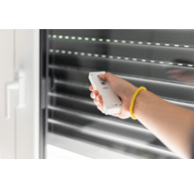 Hand bedient eine Funkfernbedienung zur Steuerung eines Rollladens an einem Fenster.