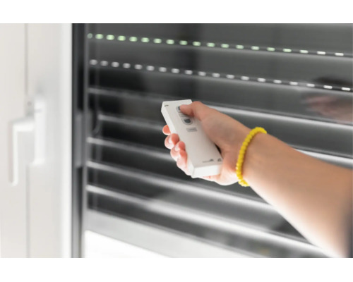 Hand bedient eine Funkfernbedienung zur Steuerung eines Rollladens an einem Fenster.