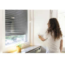 Eine Frau bedient einen elektrischen Rollladen an einem Fenster mit einem Wandschalter im Innenbereich.