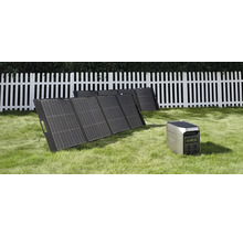 Tragbares Solarpanel Set mit Powerstation auf einer Wiese vor einem weißen Holzzaun.