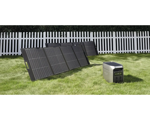 Tragbares Solarpanel Set mit Powerstation auf einer Wiese vor einem weißen Holzzaun.