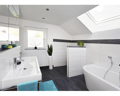 Modernes Badezimmer mit Dachschräge, weiß gefliesten Wänden, dunklen Bodenfliesen, Doppelwaschtisch und freistehender Badewanne unter Dachfenster.