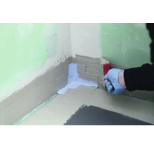 Hand mit Handschuh streicht Dichtband in eine Wandecke ein um eine Verbundabdichtung vorzubereiten.