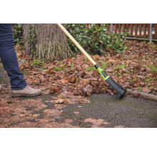 Person kehrt trockenes Laub von einem Gartenweg mit einem Laubbessen mit Holzstiel.
