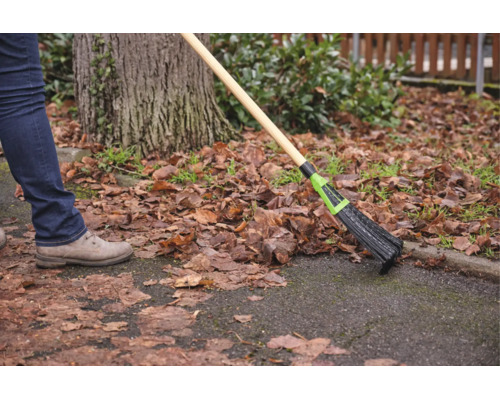 Person kehrt trockenes Laub von einem Gartenweg mit einem Laubbessen mit Holzstiel.