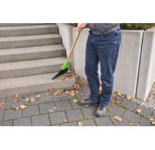 Person kehrt mit einem Besen mit Holzstiel und Kunststoffborsten trockenes Laub von einer Betontreppe und einem gepflasterten Boden.