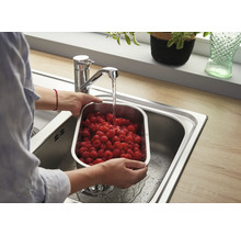 Person wäscht frische Himbeeren in einem Edelstahl Sieb in einer Küchenspüle unter einem modernen Einhebelmischer.