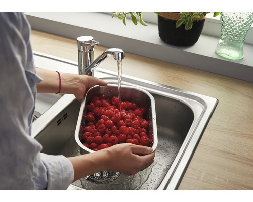 Person wäscht frische Himbeeren in einem Edelstahl Sieb in einer Küchenspüle unter einem modernen Einhebelmischer.