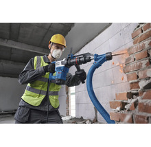 Handwerker mit Schutzausrüstung verwendet einen Bosch Bohrhammer mit Staubabsaugung beim Meißeln in einer Ziegelwand auf einer Baustelle.