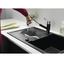 Eine moderne schwarze Küchenspüle mit ausziehbarer Küchenarmatur, an der eine Hand Wasser über die Abtropffläche fließen lässt.
