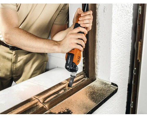 Handwerker verwendet ein Multifunktionswerkzeug zum Bearbeiten eines Fensterrahmens aus Holz.